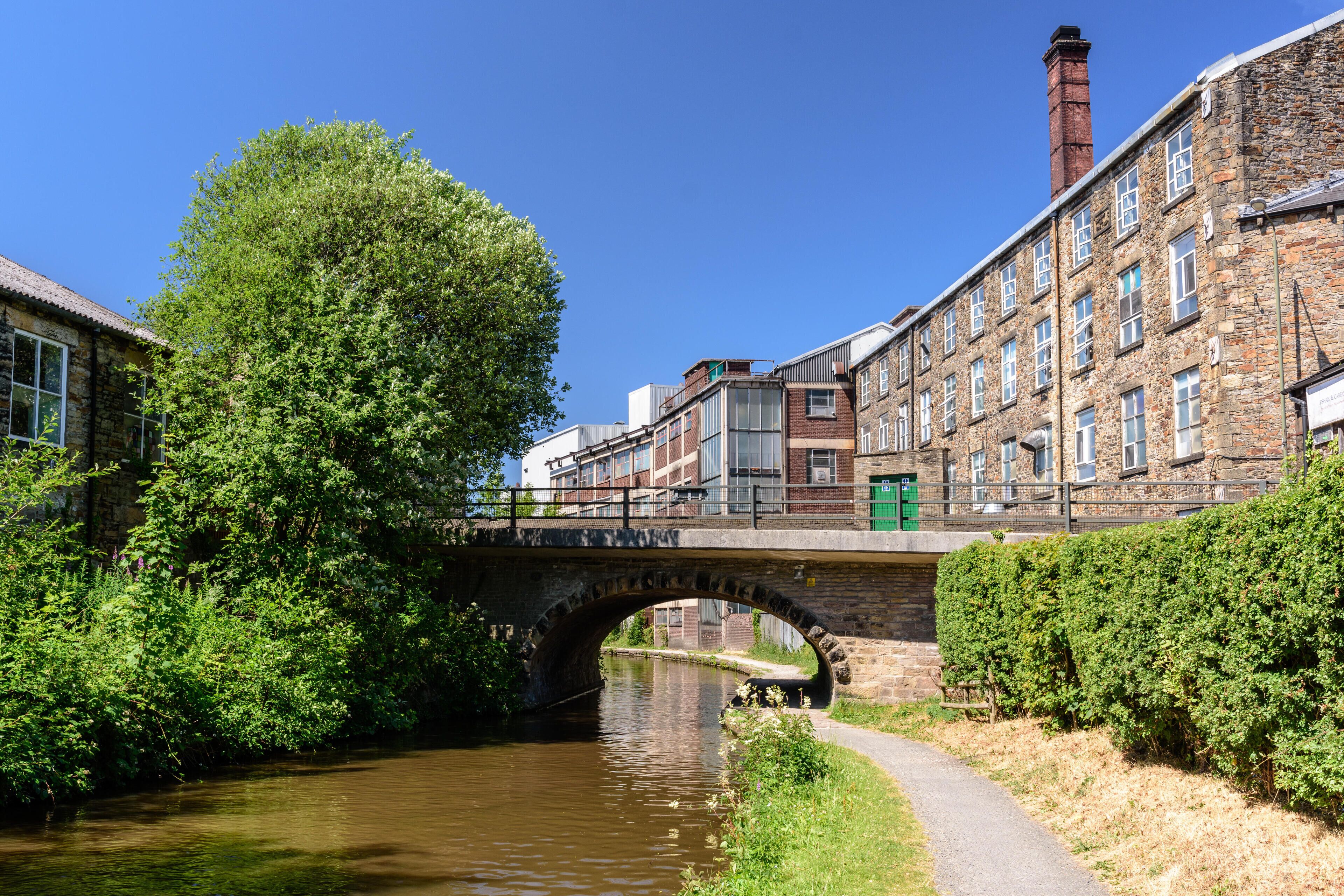A stone bridge over a river, surrounded by greenery and historic buildings.