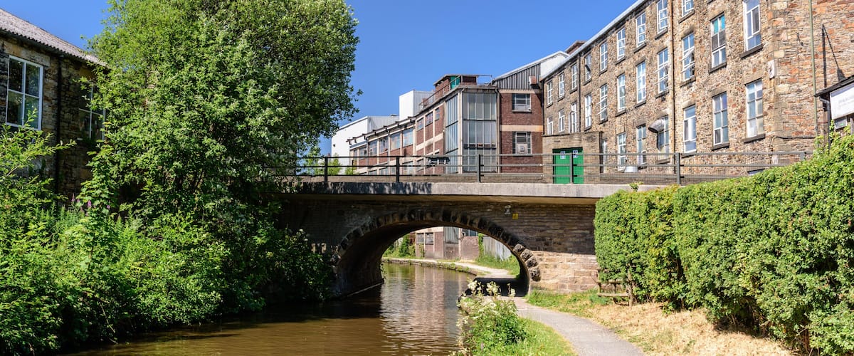 A stone bridge over a river, surrounded by greenery and historic buildings.