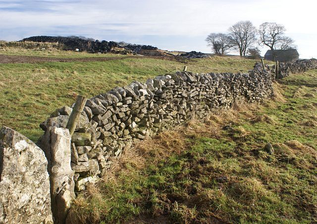 Farm track and barn A grassy farm track leads to a barn. Old tyres hold down sheeting covering winter feed. A footpath crosses the track via the squeeze stile in the foreground.