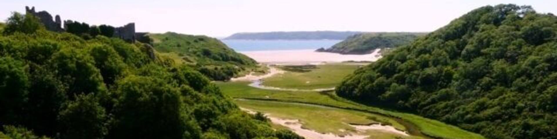 A coastal landscape with a castle on a hill, a river, and a beach.