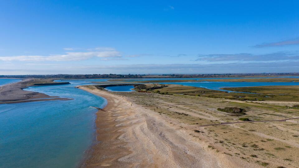 A coastal landscape with a sandy beach, a river, and a distant tree line.