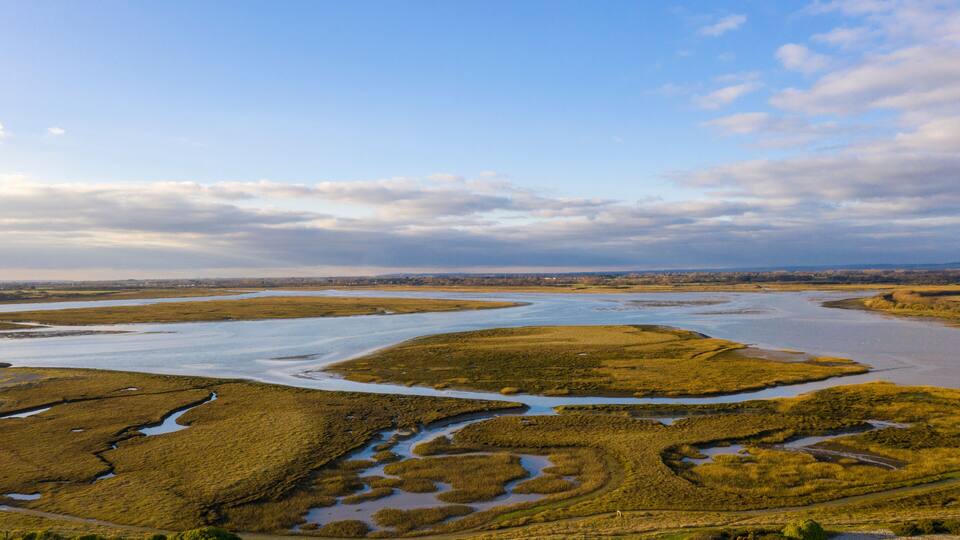 A coastal landscape with tidal flats, water channels, and distant shoreline.