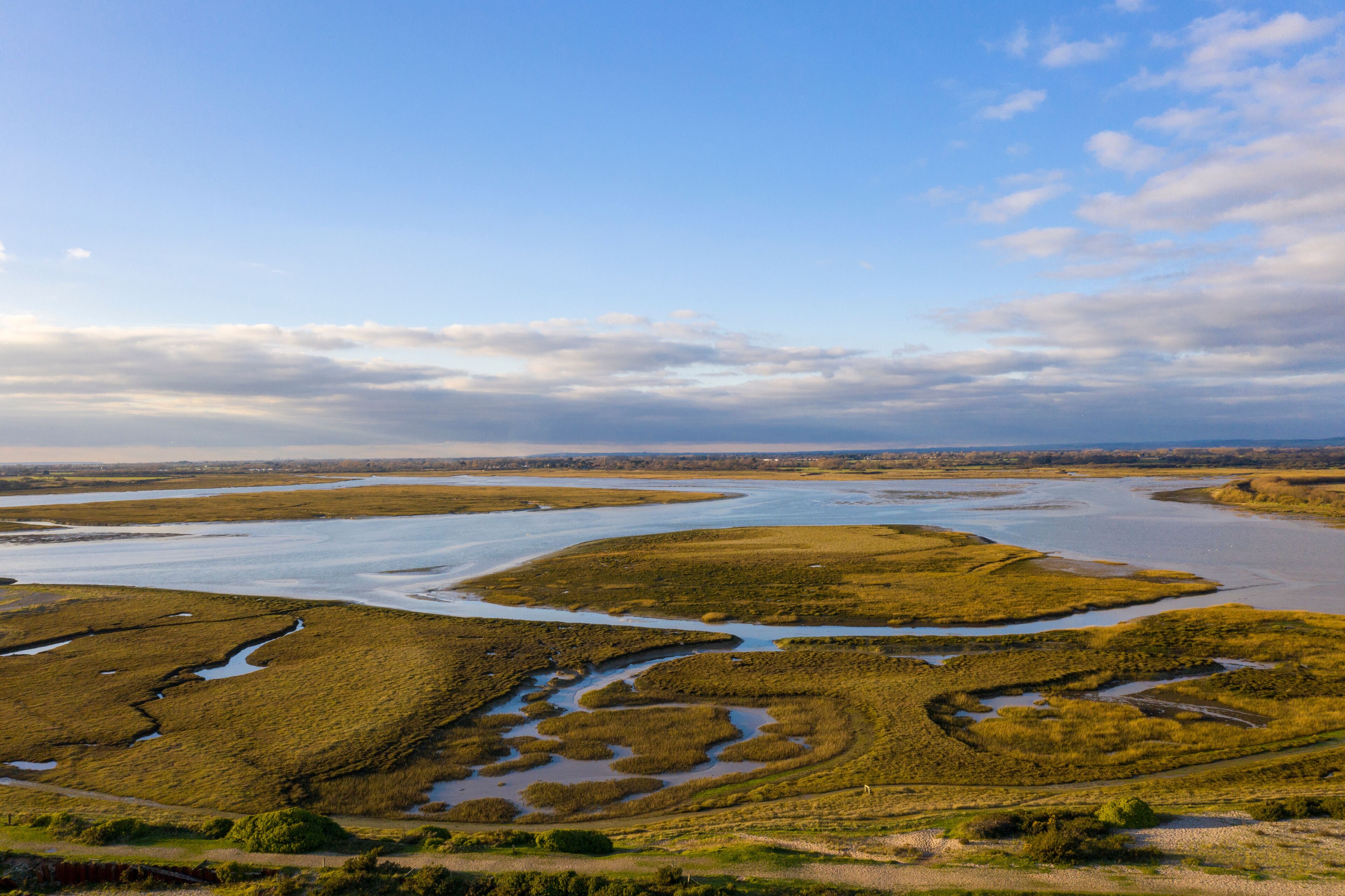 A coastal landscape with tidal flats, water channels, and distant shoreline.