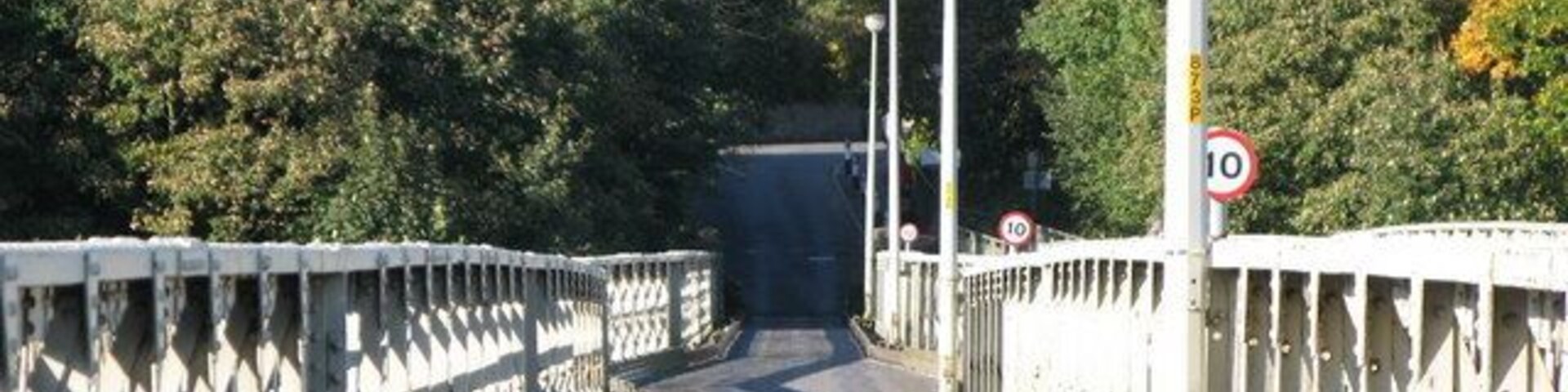 Uma ponte para pedestres com uma placa de limite de velocidade de 10, rodeada por árvores.