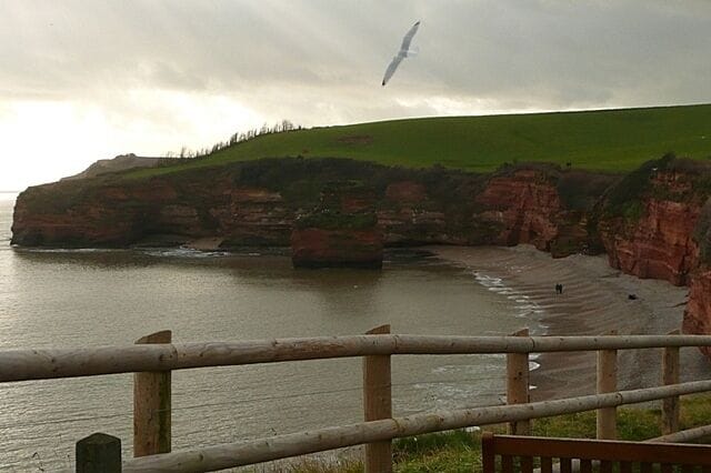A coastal landscape with cliffs, a beach, and a wooden fence.