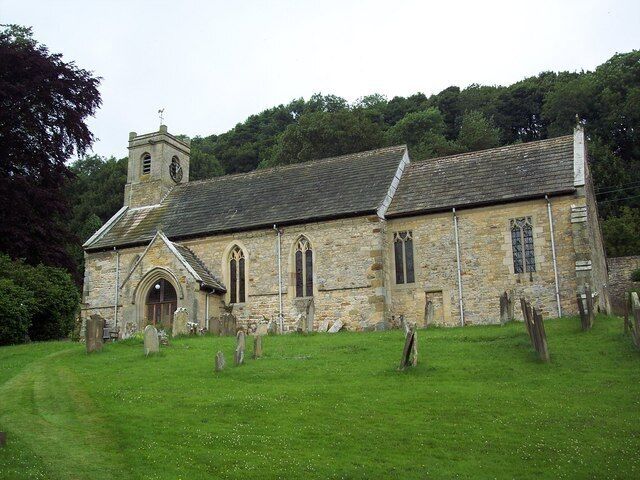 A stone church with a bell tower and a grassy cemetery in the foreground.
