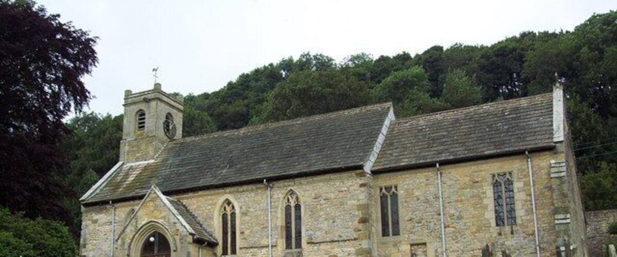 A stone church with a bell tower and a grassy cemetery in the foreground.