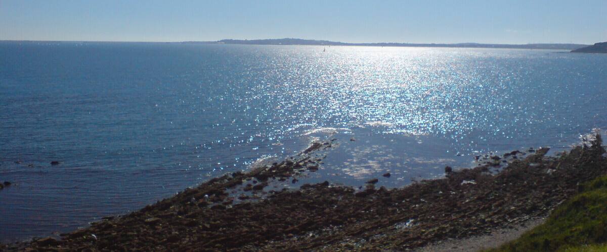 A coastal landscape with a rocky shoreline and calm sea under a clear sky.