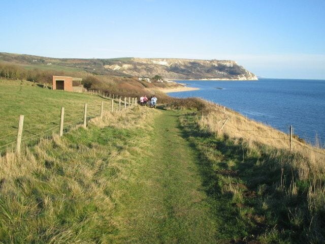 A coastal path with a fence, a small structure, and a beach in the background.