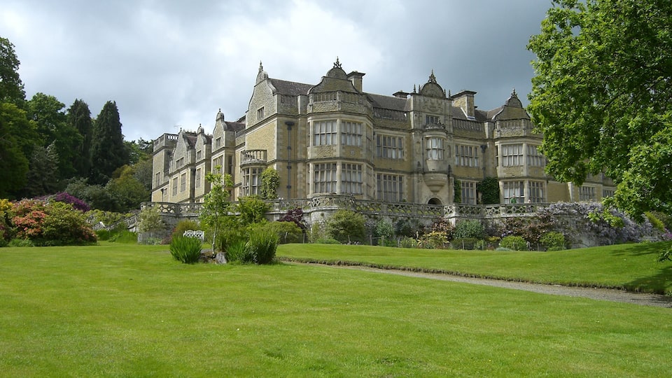 A large, historic building with a well-maintained lawn and garden in front.