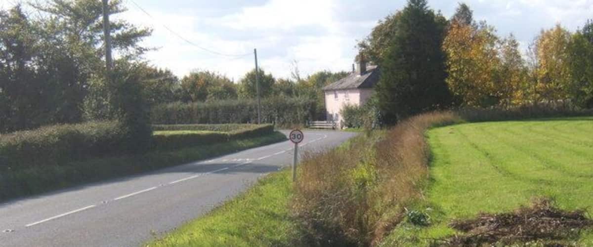 A rural road with a speed limit sign, a grassy field, and a house in the background.