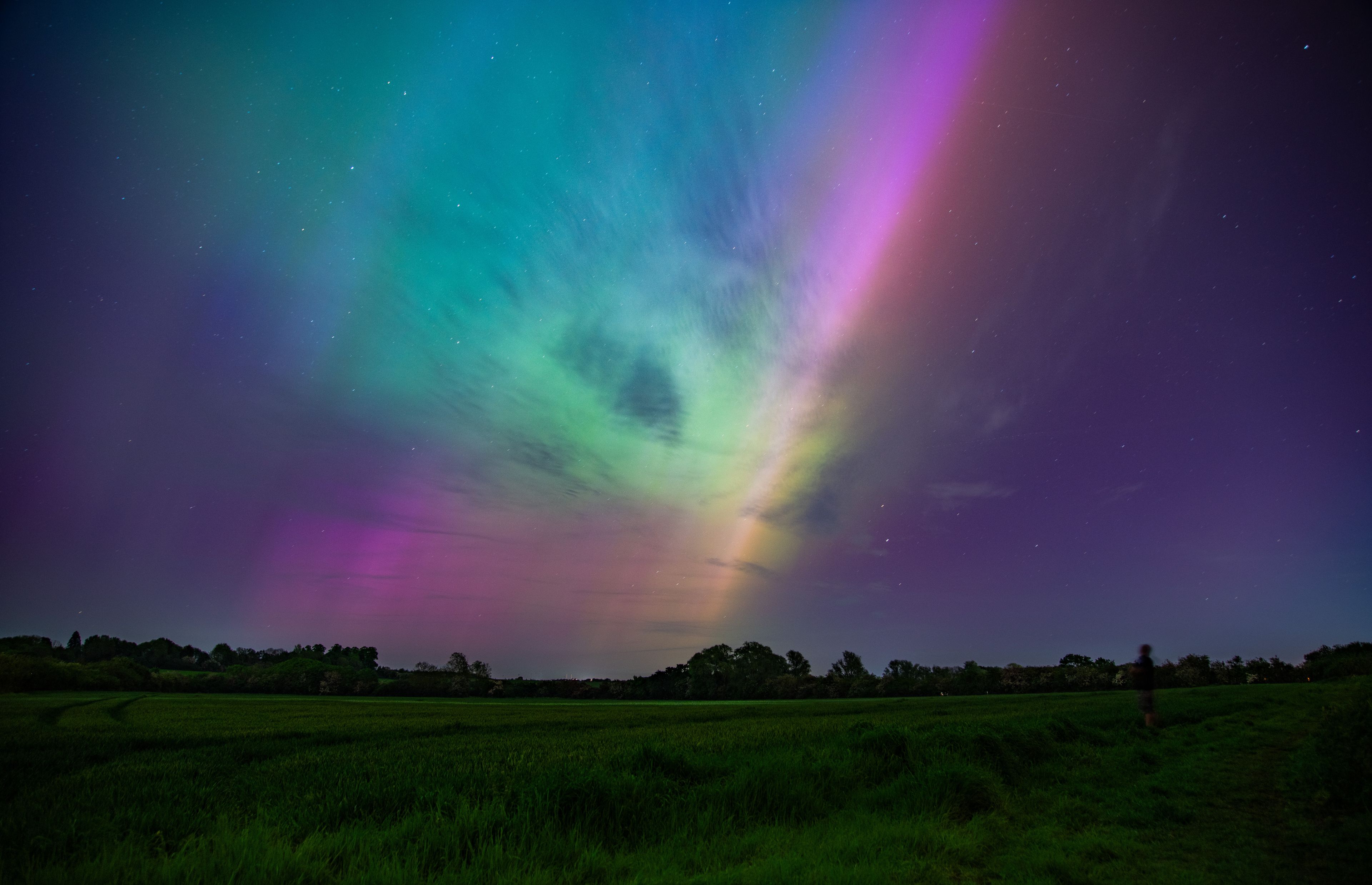 Un campo bajo un cielo nocturno con la aurora boreal.