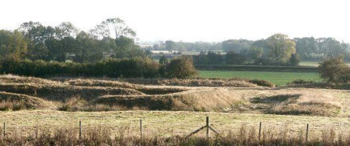 A rural landscape with rolling fields, a fence, and trees in the background.