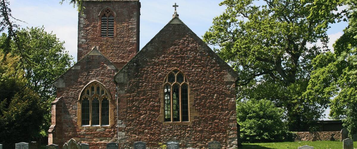 A historic church with a tower and arched windows, surrounded by a cemetery with headstones.