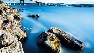 A suspension bridge over calm water with rocky shores.