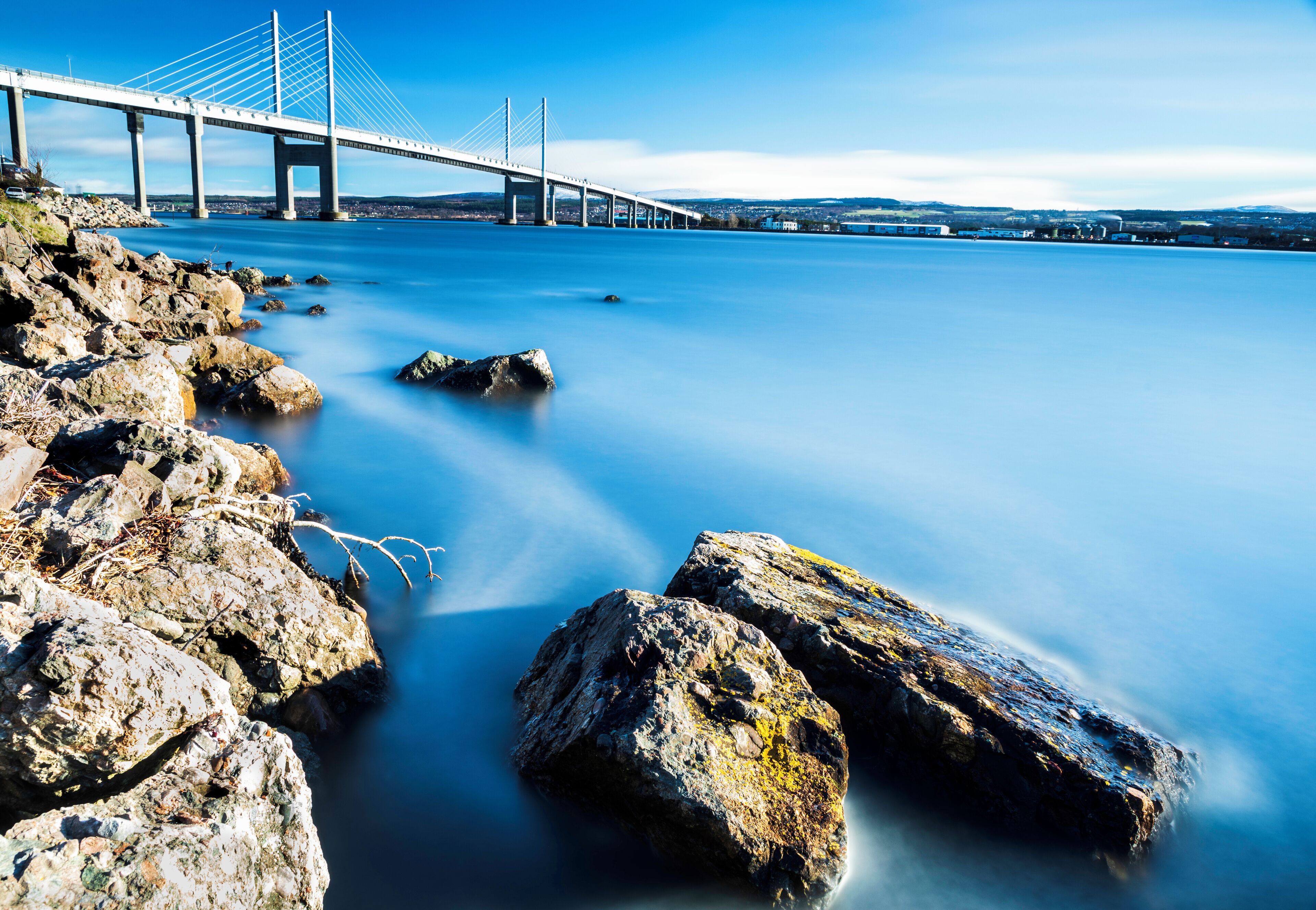 A suspension bridge over calm water with rocky shores.