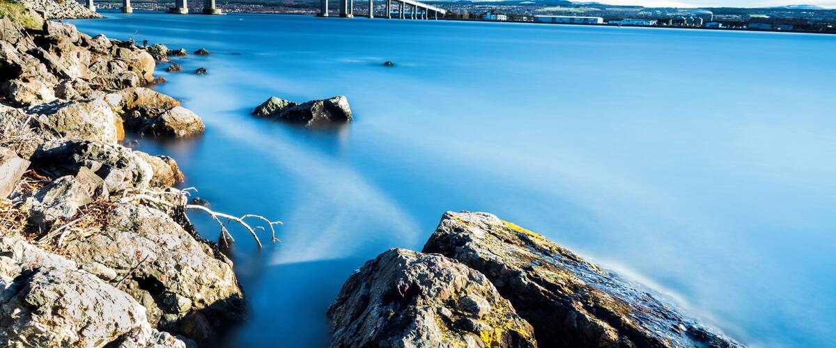 A suspension bridge over calm water with rocky shores.
