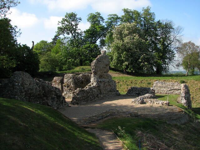 Ancient stone ruins with a grassy hill and trees in the background.