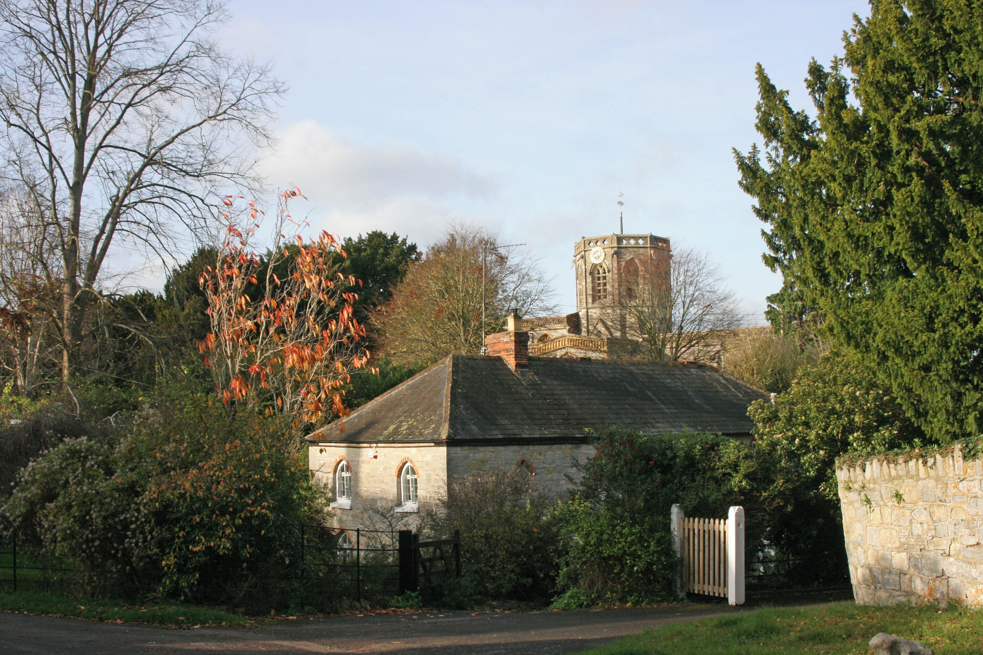 A stone building with a clock tower, surrounded by trees and a stone wall.
