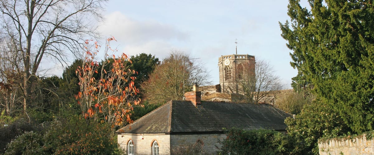 A stone building with a clock tower, surrounded by trees and a stone wall.