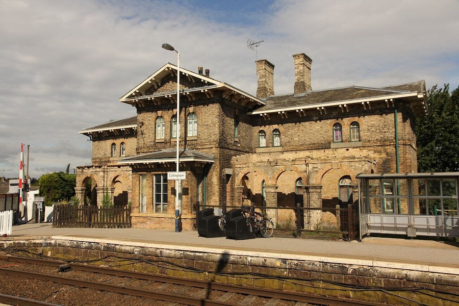 Una storica stazione ferroviaria con un grande edificio in mattoni, finestre ad arco e un binario dotato di recinzione.