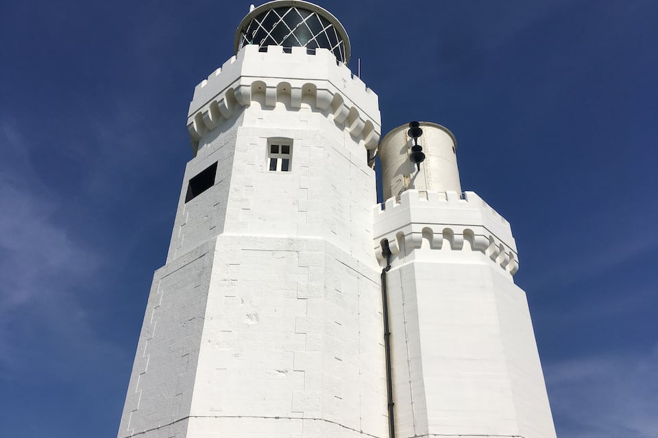 Una torre blanca con un reloj y una cúpula contra un cielo azul despejado.