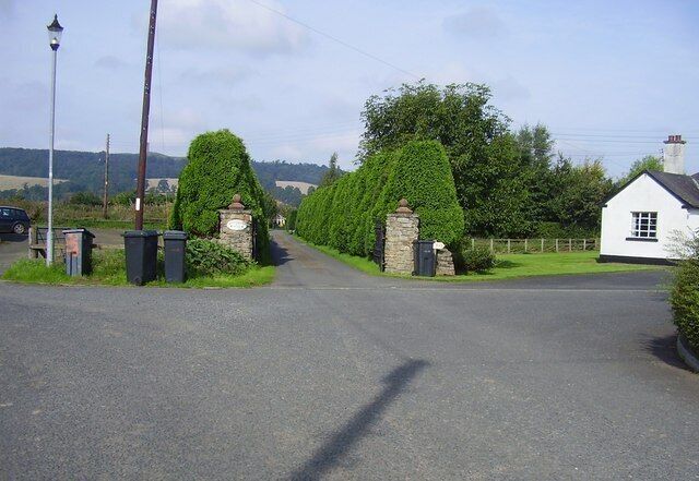 A rural road with a white house and stone gate.