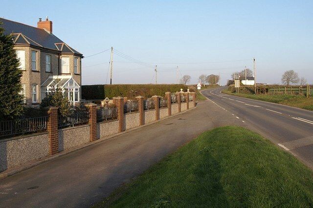 A two-lane road with a brick wall and a house on the left.