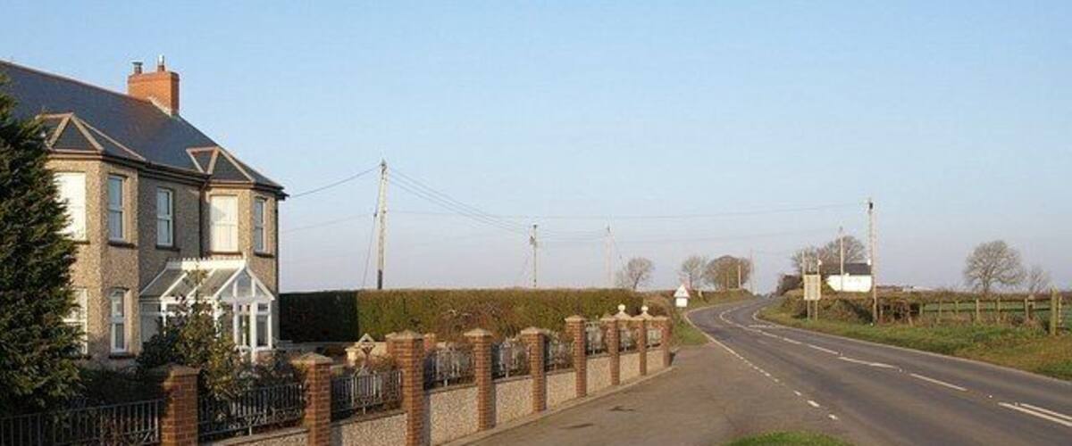 A two-lane road with a brick wall and a house on the left.
