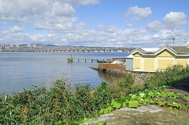 A waterfront with a bridge, a yellow building, and a stone pier.
