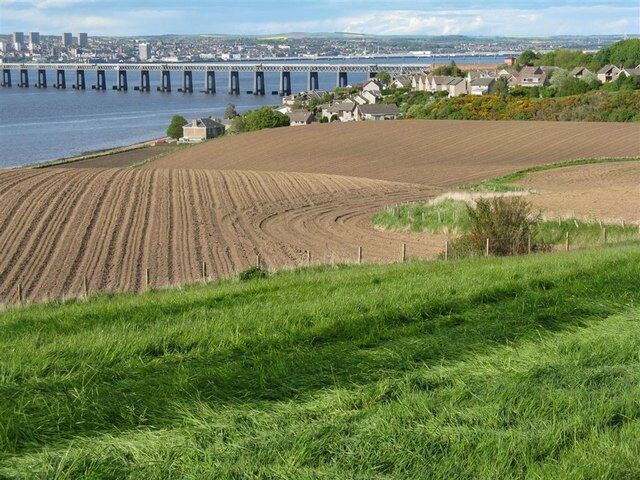 A coastal landscape with a bridge, fields, and houses.