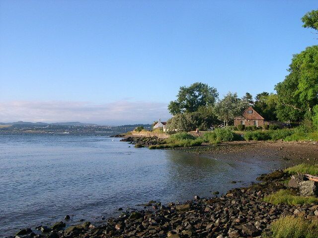 A calm lake with a rocky shoreline, a small house, and trees in the background.