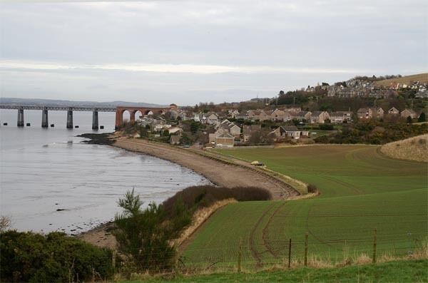 A coastal town with a bridge, houses, and fields.