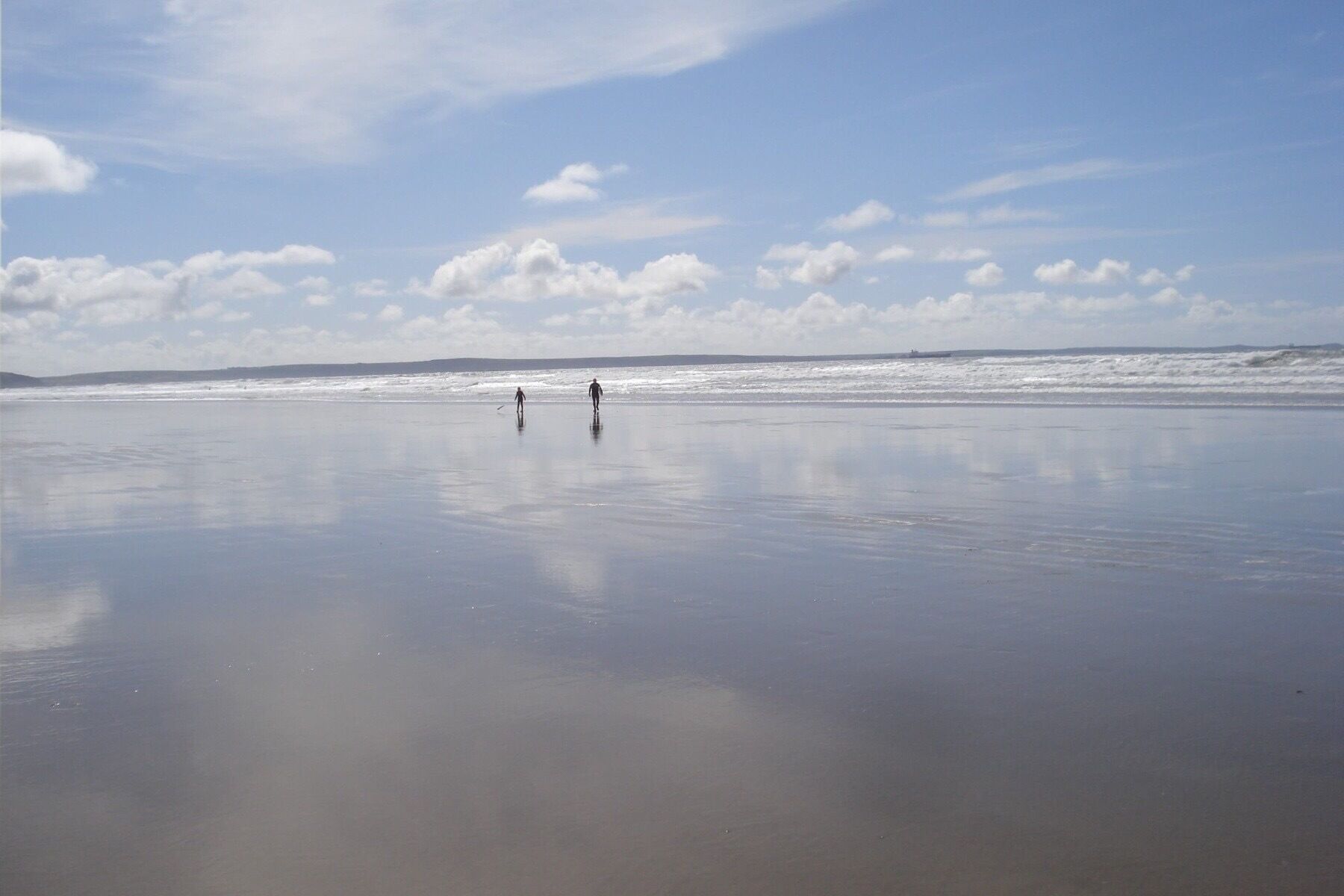 A wide, calm beach with two people walking towards the ocean.