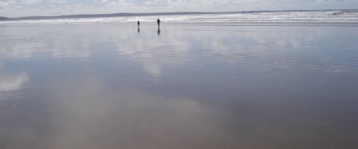A wide, calm beach with two people walking towards the ocean.