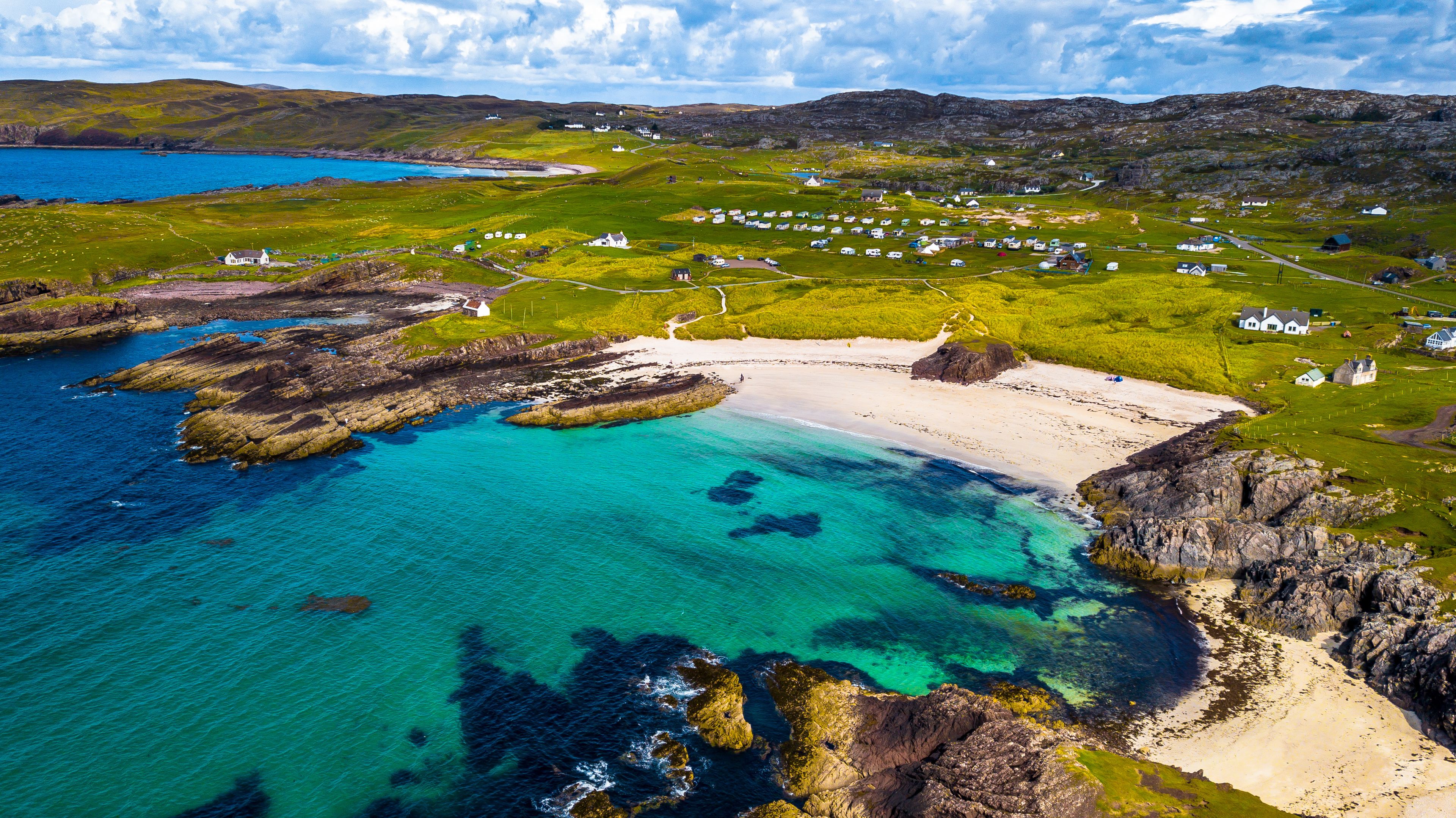 A coastal landscape with clear turquoise waters, rocky shores, and a village with white houses.