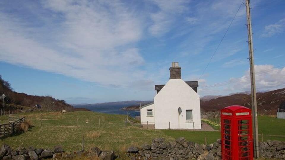 A white house with a red telephone booth in a rural setting.