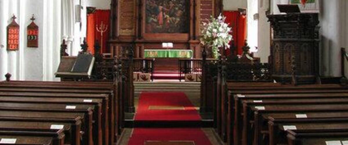 Un pasillo con bancas, una alfombra roja y un altar de madera con un vitral.
