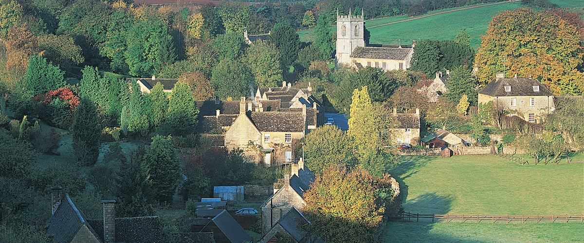 A village with historic stone buildings, a church, and rolling hills in the background.