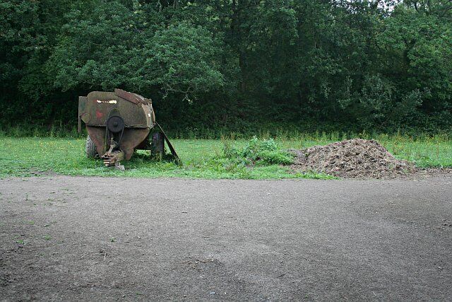 An old 'muck spreader' This farm machinery was seen in a small field between the road and woodland. On the right is a pile of dirty straw, just the sort of thing which this machine might have thrown onto the fields.