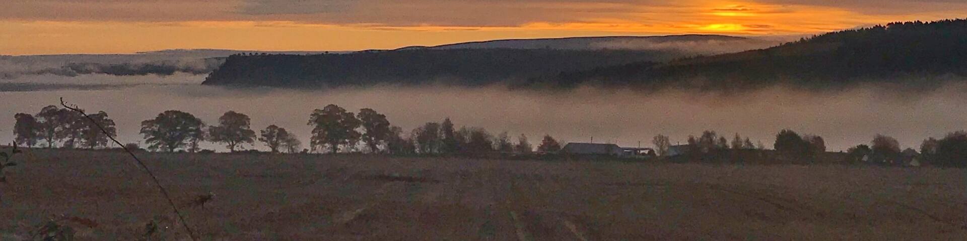 A sunset over a hilly landscape with a misty foreground.