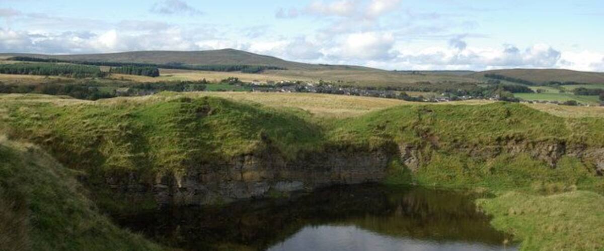 A grassy landscape with a small pond and distant hills.