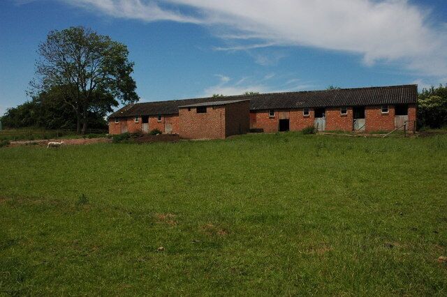 A brick building with a sloped roof in a grassy field.