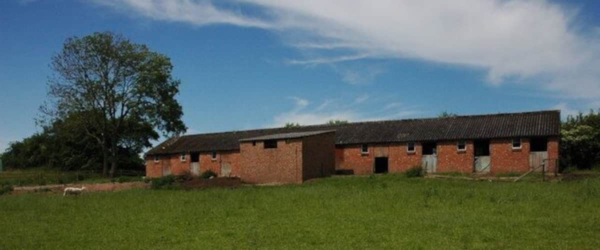A brick building with a sloped roof in a grassy field.