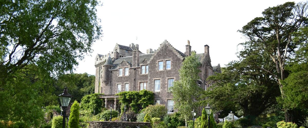 A large, historic stone building with a well-manicured lawn and lush greenery.