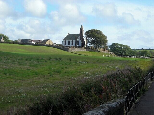 Una iglesia con una torre alta, un campo cubierto de hierba y un muro de piedra.