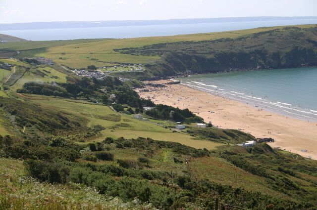 A coastal landscape with a beach, rolling hills, and a distant view of the sea.