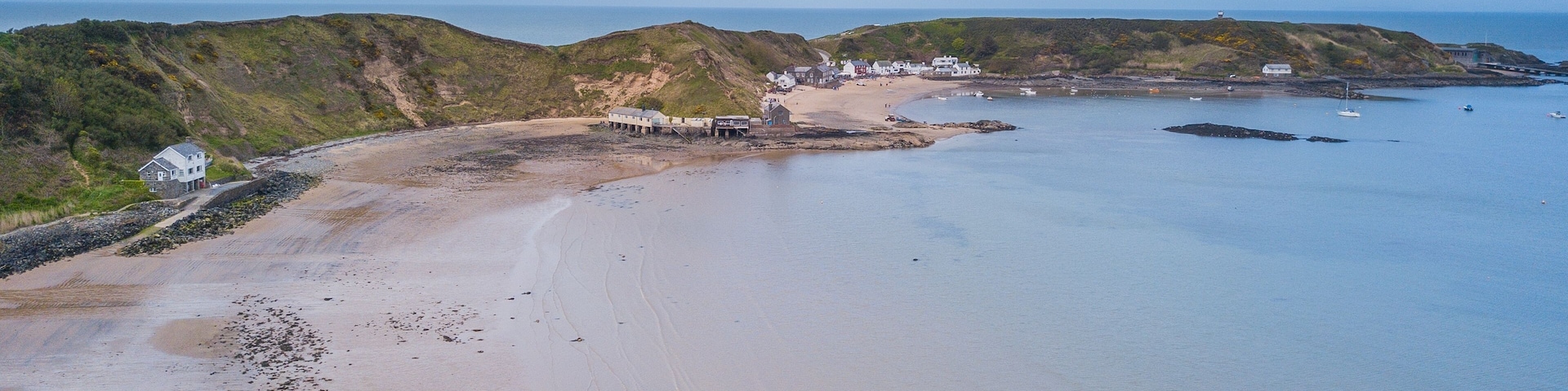 Un paisaje costero con una playa arenosa, afloramientos rocosos y un pequeño asentamiento con edificios.