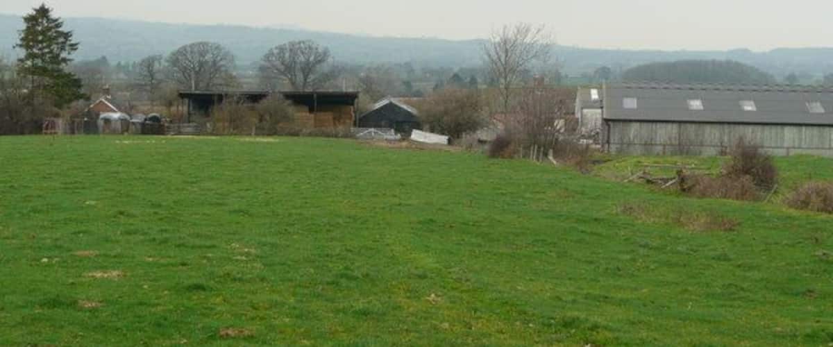 A rural landscape with a green field, several barns, and distant mountains.