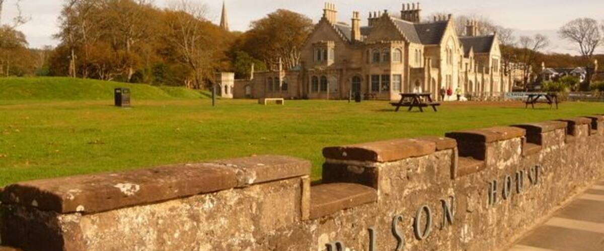 A stone wall with 'Garrison House' engraved on it, a grassy field, and a large building in the background.